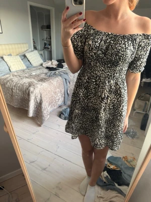 Svartvit offshoulder kortklänning - Supersöt kort klänning med svartvitt abstrakt mönster. Offshoulder-modell med puffiga korta ärmar och smockad överdel som ger en snygg passform. 