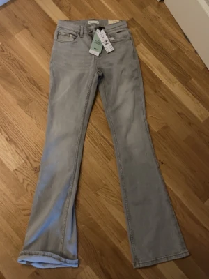 Lågmidjade bootcut jeans från Gina Tricot - Snygga lågmidjade bootcut jeans från Gina Tricot i en ljusgrå tvätt. Modellen heter Perfect Jeans och är tillverkad av 50% ekologisk bomull. Klassisk femficksdesign med dragkedja och knapp framtill. Perfekt för dig som gillar retrovibbar och relaxed stil.