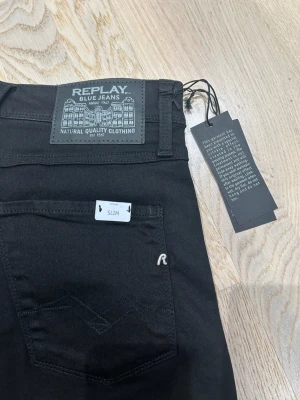 Svarta Replay Anbass slim jeans - Säljer ett par svarta Replay Anbass jeans med slim passform. Klassisk femficksdesign, snygga detaljer med Replay-logga på bakfickan och patch vid midjan. Jeansen är tillverkade i stretchigt bomullsmaterial för skön känsla och sitter tajt över benen. HELT HELT SPRILLANS NYA med taggar och etiketter‼️om ni har frågor eller funderingar tveka inte på att kontakta mig för information‼️