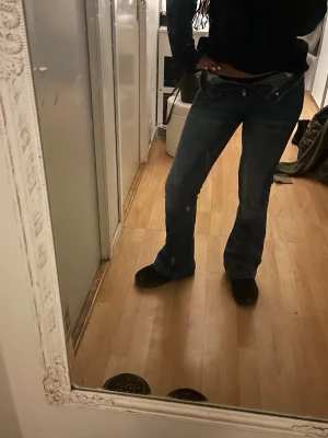 Blå h&m bootcut jeans hög midja - Säljer ett par blå h&m  jeans med bootcut och hög midja. Jeansen har klassisk femficksdesign, dragkedja och knapp framtill. Materialet är jeans med snygga slitningar och tvättade detaljer. Perfekt för dig som gillar retrovibe och avslappnad stil.