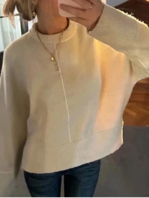 Beige stickad tröja från Zara - Säljer en beige stickad tröja från Zara i storlek XS. Tröjan har en rak passform, lång ärm och ribbade muddar vid hals, ärmslut och nederkant. Snygg detalj med en söm framtill som ger en clean look. Perfekt till jeans eller kjol.