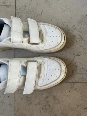 Vita sneakers Acne Studios med kardborre - Säljer ett par vita sneakers från Acne Studios med två breda kardborreband. Skorna har en tjock och beige sula och Acne Studios-logga på sidan samt den klassiska smiley-detaljen bak. Tillverkade i skinn med rund tå och platt sula. Är i storlek 37 men funkar för mig som vanligtvis har 38! Ytligt smuts förekommer på bilden, men det tvättar jag såklart bort innan dom skickas isåntfall!