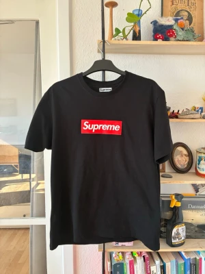 Supreme svart box logo t-shirt - Supreme t-shirt i svart med den klassiska röda box loggan framtill. Gjord i 100% bomull för en skön och avslappnad känsla. Perfekt för dig som gillar streetwear och vill sticka ut med en ikonisk look.