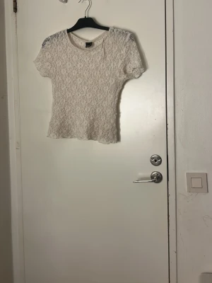 Vit spetsblus från Gina Tricot nytt skick  - Säljer en vit blus från Gina Tricot med korta ärmar och rund hals. Blusen är helspets med ett fint blommigt mönster och har en lätt transparent look. Perfekt att styla med jeans eller kjol för en fräsch vibe. 