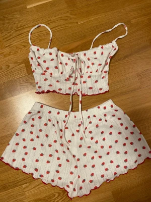 gulligt pyjamasset med jordgubbar på - vitt pyjamasset (shorts och croppat linne) med jordgubbsmönster och röd kant! materialet är stretchigt och axelbanden till linnet är justerbara. okänt märke