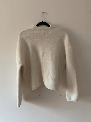 Vit stickad tröja med hög krage - Säljer en enkel och stilren vit stickad tröja med hög krage. Tröjan har långärmade och en loose passform som ger en chill vibe. Perfekt för lager-på-lager under kyliga dagar. Materialet är mjukt och känns skönt mot huden. 