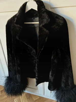 Svart pälsjacka från Meotine - Säljer en svart pälsjacka från Meotine, modell Dagmar Jacket, i 100% äkta lammull. Jackan har fluffiga ärmslut, klassisk krage och knappar framtill. Storlek M men passar även S. Nypris 5500 DKK / ca 8000 SEK