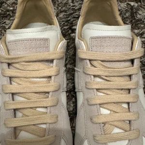 Maison Margiela gats - (nypris 5999❌ mitt pris 1899✅)  Maison Margiela sneakers i beige och vitt med klassisk gummisula. Ovandel i skinn och mocka, beige snörning och diskret logotyp på plösen och sulan. Snygg minimalistisk design som passar till allt.