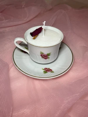 Doftljus i en tekopp i en vit färg med röda blommor på nr 1 - Det här ljuset är gjort av återanvändbara material. Tekoppen är köpt secondhand och stearinet är från kyrkor som tänkte slänga det. Det här ljuset har en svag doft utav vanilj, så känsliga även kan använda det. Det finns även fler ljus med denna design på hemsidan, om man vill köpa sets. Det här ljuset har även torkade blommor på och kanel 