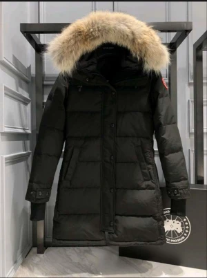 Svart vinterjacka med päls från Canada Goose - Säljer en svart lång vinterjacka från Canada Goose med fluffig päls på huvan och klassisk logga på ärmen. Jackan har dragkedja och knappar framtill, långa ärmar och flera fickor. Perfekt för kalla vinterdagar och riktigt snygg stil. Helt ny med prislappen på