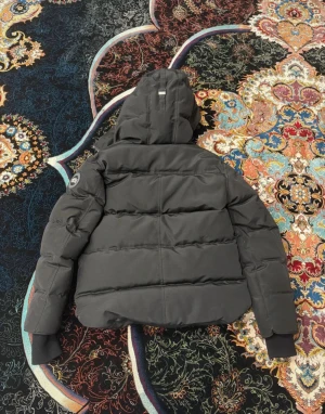 Svart pufferjacka från Canada Goose - Svart pufferjacka från Canada Goose med huva och snyggt märke på ärmen. Jackan har quiltad design, dragkedja och muddar vid ärmslut. Perfekt för kalla dagar och har en clean, modern look. Modellen är Fusion S/P.