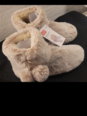  Helt nya Beige fluffiga tofflor med bollar 36 - 37 -  Helt nya Supermysiga beige tofflor från Clevé med fluffigt pälsmaterial och söta bollar som detalj vid sidan. De har en rund tå och är fodrade för extra värme, perfekta för julklapp 36 37 storlek 