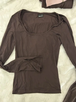 Brun långärmad topp Gina Tricot XS - Säljer en brun långärmad topp från Gina Tricot i storlek XS. Toppen har en djup rundad halsringning och är tillverkad i mjuk bomull. Perfekt att styla med jeans eller kjol för en enkel och snygg look.