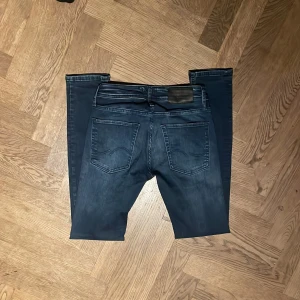 Mörkblå jeans Jack & Jones - Säljer ett par mörkblå  jeans från Jack & Jones med snygg tvätt och slitningar på benen. Klassisk femficksmodell med dragkedja och knapp i midjan. Jeansen har en smal passform och är tillverkade i stretchig bomull för extra komfort.