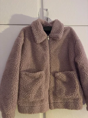 Beige teddyjacka från New Look - Mysig teddyjacka i rosa brun  från New Look med fluffig yta och två stora fickor framtill. Jackan har klassisk krage och stängs med dragkedja. Perfekt för dig som gillar chill och comfy stil under höst och vinter.