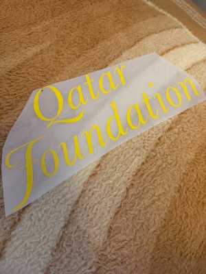 Qatar Foundation tryck i gult - Säljer ett Qatar Foundation tryck i gul färg, perfekt för att stryka på en fotbollströja eller hoodie. Trycket är gjort i syntetmaterial och har en snygg, klassisk font. Passar dig som vill ha en unik detalj på dina kläder.