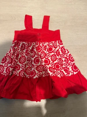 Röd och vit klänning Polarn O. Pyret - Söt klänning från Polarn O. Pyret i storlek 92. Klänningen har breda axelband, två röda knappar framtill. mjuk bomull. Kjoldelen är vit med rött blommigt mönster . 