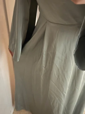 Ljus långklänning med vida ärmar - Säljer en elegant ljus långklänning med vida långärmar och mjukt fall. Klänningen har en enkel, stilren design med markerad midja och är tillverkad i ett slätt, lätt material som ger ett snyggt flöde. Perfekt för dig som gillar minimalistisk stil. Funkar till bal eller en helt vanlig fest.