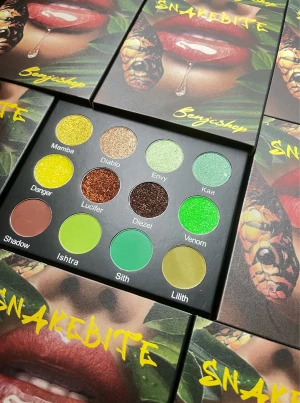 Snakebite ögonskuggspalett Benjii shop - Snakebite ögonskuggspalett med 12 färgstarka nyanser i grönt, gult, brunt och koppar. Paletten innehåller både matta och skimrande skuggor, perfekta för kreativa och färgglada looks. Namngivna skuggor som Mamba, Venom och Sith. Snygg förpackning med handgjort ormomslag.