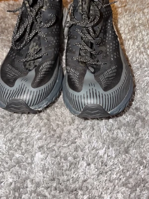 Svarta Merrell sneakers strl 46,5 - Säljer ett par svarta Merrell sneakers med grå detaljer och mönstrad mesh. Skorna har snörning och en robust Vibram-sula som ger bra grepp. Perfekta för dig som gillar att vara aktiv och vill ha snygga och funktionella skor.