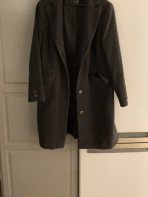 Svart rock från Etage - Snygg svart rock från Etage med klassisk krage och två framfickor. Jackan har knappar framtill och på ärmsluten, vilket ger en stilren look. Perfekt för dig som gillar enkel och tidlös design. Materialet känns mjukt och har en ullkänsla.