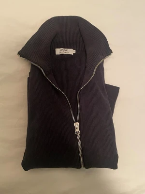 Mörkblå ribbad kofta från Ljung - Säljer en mörkblå ribbad kofta från Ljung by Marcus Larsson i storlek S. Koftan har lång ärm, hög krage och hel dragkedja framtill. Materialet är stickat och ger en skön och stilren känsla. Perfekt för dig som gillar minimalistisk design och snygga detaljer.