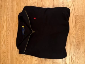 Ralph lauren half zip  - Snygg och tidlös Polo Ralph Lauren-tröja i klassiskt svart – ett självklart val för dig som vill ha stil med kvalitet. Storlek L men passar också M   Tröjan har en hel dragkedja, mjukt och bekvämt material samt den ikoniska röda Polo-loggan broderad på bröstet, vilket ger ett exklusivt och elegant intryck. Perfekt att bära både till vardags och vid mer uppklädda tillfällen. Passar lika bra över en skjorta som till en t-shirt.