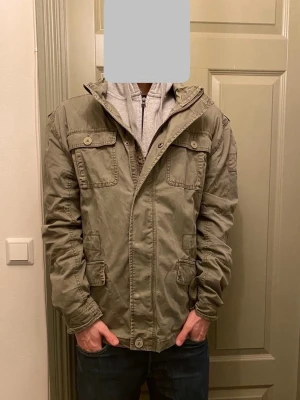 Olivgrön fieldjacka från Brandit - Säljer en riktigt fet olivgrön fieldjacka från Brandit med flera fickor framtill, både med knapp och lock. Jackan har dragkedja och knappar framtill. Vid funderingar, fråga på! 