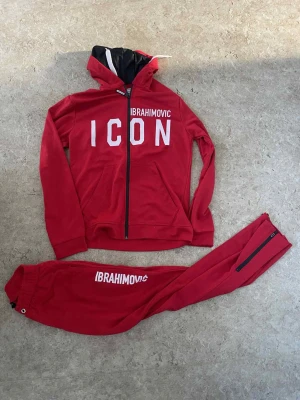 Röda mjukisbyxor Ibrahimovic x Dsquared2 - Säljer ett par röda mjukisbyxor med trycket 'IBRAHIMOVIC' på benet. Byxorna har resår i midjan, dragkedja vid benslut och är gjorda i mjukt bomullsmaterial. Snygg streetwear-look som matchar med hoodie från samma kollektion.