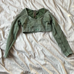 Olivgrön croppad topp från Bo+Tee - Säljer en olivgrön croppad topp från Bo+Tee med lång ärm och ribbad struktur. Toppen har en snygg, formad urringning och är tillverkad i stretchigt material som sitter tight. Perfekt för dig som gillar sportig och trendig stil.  Väldigt stretchig. Om du har större bröst än normalt kan den bli för liten för dig. Storlek L. Från Bo+tee 