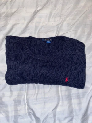 Marinblå stickad tröja Polo Ralph Lauren - Snygg marinblå stickad tröja från Polo Ralph Lauren i storlek L. Tröjan har ett klassiskt kabelstickat mönster och rund hals. På bröstet finns den ikoniska röda Polo-loggan broderad. Perfekt för dig som gillar stilrena och tidlösa plagg. Nypris 1600kr | Säljer för 300 men kan gå ner | Den är lite uttöjd i kragen |
