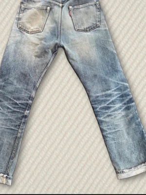 Vintage denime jeans - Säljer ett par denime i ljusblå tvätt med coola slitningar och trasiga detaljer framtill. Jeansen har raka ben, fem fickor och den ikoniska röda Levi's-taggen bak. Perfekt för dig som gillar en avslappnad och trendig streetstil.