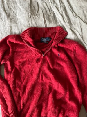 Röd half zip tröja från Polo Ralph Lauren - Säljer en röd långärmad tröja från Polo Ralph Lauren med ribbad krage och muddar. Tröjan har half zip-dragkedja och är tillverkad i 100% bomull. Klassisk logga broderad på bröstet. Perfekt för dig som gillar stilrena och bekväma plagg.