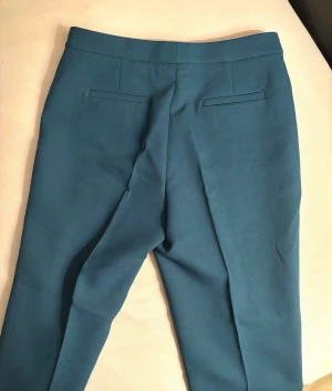 Mörkblå kostymbyxor med dragkedja - Snygga mörkblå kostymbyxor med smal passform och klassiska fickor bak. Byxorna har en stilren design med dold dragkedja fram och är tillverkade i ett slätt material som ger en clean look. Perfekta för dig som gillar en enkel och modern stil.