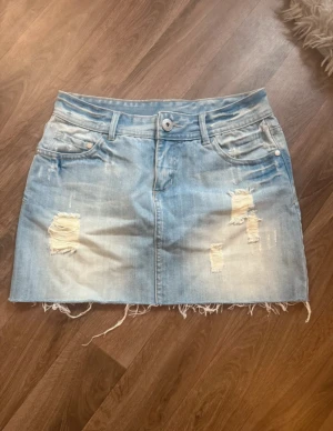 Blå jeanskjol med slitningar Str S - Säljer en kort jeanskjol i ljusblå denim med slitna detaljer och fransig nederkant. Kjolen har klassiska fickor fram och bak samt hällor för bälte. Super snygg💕