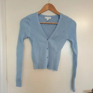 Ljusblå ribbad kofta  - Säljer en ljusblå ribbad kofta från H&M med v-ringning och knappar framtill. Perfekt för lager-på-lager och ger en stilren look. Passar bra till både jeans och kjol. 💙