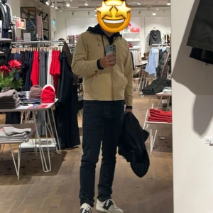 Beige jacka från Polo Ralph Lauren - Stilren beige jacka från Polo Ralph Lauren med klassisk krage, dragkedja framtill och blå broderad logga på bröstet. Rutigt innerfoder ger en snygg kontrast. Jackan har långa ärmar med knappar vid ärmslut och justerbara band i midjan.