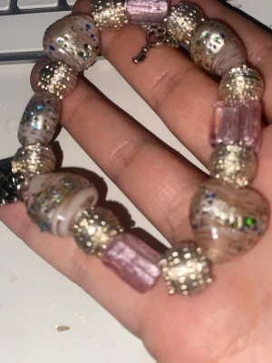 Glittrig pärlarmband med dream-tag - Unikt armband med stora glittriga pärlor i rosa och silver, dekorerat med färgglada prickar och detaljerade silverkulor. Armbandet har en metallbricka med texten 'dream' och en liten nyckelberlock. Perfekt för dig som gillar statement-smycken och färg.