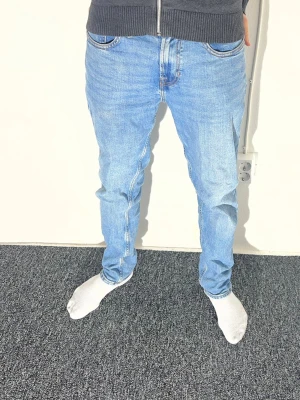 Ljusblå jeans från Zara, storlek 30 - Säljer ett par ljusblå jeans från Zara med klassisk femficksdesign och raka ben. Jeansen har normal passform och är tillverkade i bomullsmaterial. Snygga kontrastsömmar och diskret logga på bakfickan. Perfekt för dig som gillar enkel och stilren denim.