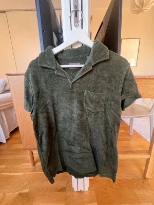 Olivgrön frotté polotopp från Berkeley - Säljer en olivgrön polotopp från Berkeley i mjuk frotté. Toppen har korta ärmar, krage och en liten bröstficka med diskret logga. Perfekt för chill dagar och har en loose passform som ger en avslappnad vibe.