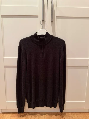 Mörkgrå half zip tröja John Henric - Snygg mörkgrå långärmad tröja från John Henric med half zip i halsen. Tröjan har en ribbad krage och är tillverkad i mjukt material som passar perfekt för kyliga dagar. Enkel och stilren design som funkar till många olika outfits.