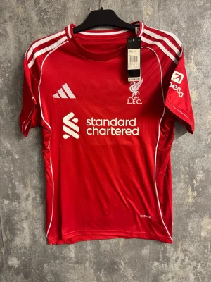 Liverpool Salah - Ny storlek S - Bilderna visar en röd Liverpool FC fotbollströja med M. Salah och nummer 11 på ryggen, tillverkad av Adidas.