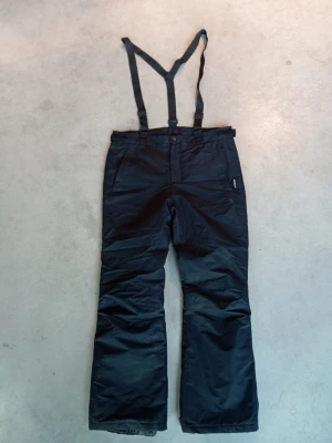 Svarta täckbyxor McKinley med hängslen - Svarta täckbyxor från McKinley i storlek Large, perfekta för vinteraktiviteter. Byxorna har justerbara hängslen, raka ben och praktiska fickor. Materialet är slitstarkt och håller dig varm under kalla dagar. Snygg och funktionell design för dig som gillar att vara ute. Använda en gång! 