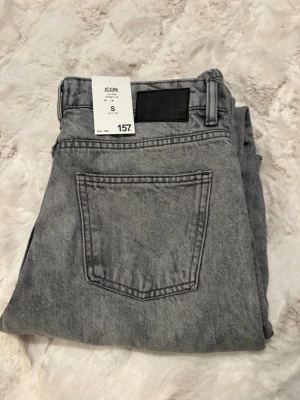 Grå low rise jeans från 157 - Säljer ett par gråa low rise jeans från 157 med raka ben och klassisk femficksdesign. Jeansen har en snygg tvättad look och silverfärgade detaljer vid knappar och nitar. Perfekta för dig som gillar en avslappnad och trendig stil.