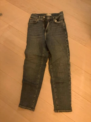 Perfect Jeans från Gina Tricot, storlek 36 - Säljer ett par klassiska blå Perfect Jeans från Gina Tricot i storlek 36. Modellen har hög midja, smal passform och raka ben. Jeansen är tillverkade i jeansmaterial med snygga detaljer som dragkedja och knappar framtill samt bakfickor.
