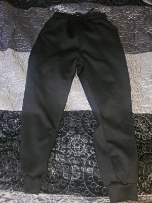 Svarta fodrade mjukisbyxor med snörning S - Mysiga svarta mjukisbyxor i storlek S med dragsko i midjan och muddar vid bensluten. Tillverkade i 100% polyester med fluffigt foder på insidan för extra komfort. Perfekta för chill dagar eller när du vill vara extra bekväm. Supervarma!