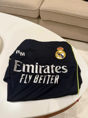 Real Madrid fotbollströja  - Mörkblå Real Madrid fotbollströja i storlek M. Riktigt snygg och skön, perfekt till alla lägen!!! Helt ny använd fåtal gånger. Pris kan diskuteras vid snabb affär!!