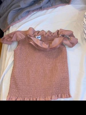 Rosa volang topp från Bubbleroom - Supersöt rosa topp från Bubbleroom i storlek M. Toppen är ärmlös och har bred volang runt axlarna samt smockad kropp för en stretchig och bekväm passform. Volangdetaljer både upptill och nedtill ger en romantisk vibe. Perfekt till sommaren!