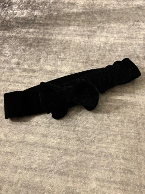 Svart sammetsbälte  med rosett - Säljer ett svart bälte i mjuk sammet med en snygg rosett framtill. Bältet har en enkel och stilren design som ger en cool touch till din outfit. Bältet är i 70cm