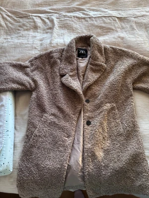 Beige teddyjacka från Zara - Säljer en beige teddyjacka från Zara med två stora fickor och knappar framtill. Jackan har en mysig, fluffig yta och bred krage som ger en chill vibe. Perfekt för dig som gillar oversized och vill ha något riktigt mjukt och varmt.